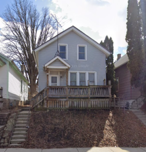 Photograph of a two-story house setback on a small hill.
