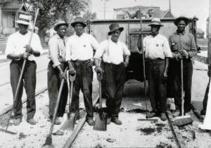Six men posing with shovels and rakes. They are standing on an under-construction railway.